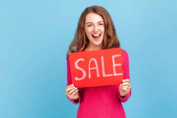 Extremely happy woman wearing pink pullover, holding Sale word and laughing loudly, feeling...