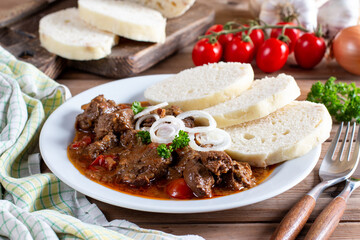 Czech traditional goulash with breaded dumpling and onion on white plate on table