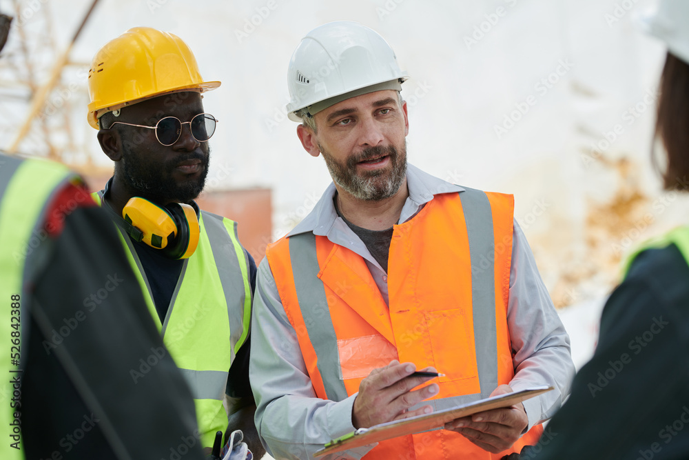 Leinwandbilder confident foreman with document and pen explaining something to subordinates or giving instructions 