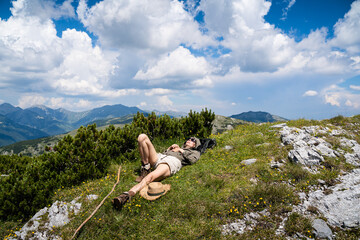 young Caucasian woman lying down and taking a rest in the grass on a mountain peak with blue sky and clouds above © macondos