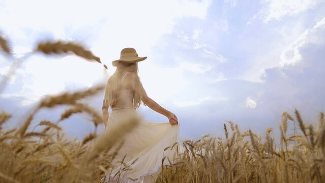 Self-sufficient woman in a summer rustical dress and hat dancing in a field of wheat