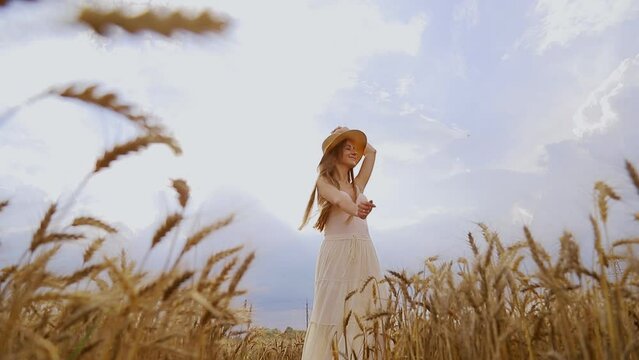 Self-sufficient woman in a summer rustical dress and hat dancing in a field of wheat