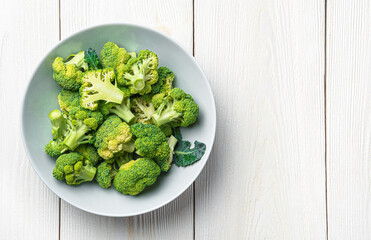 Green broccoli in a plate on a white wooden background. Healthy, dietary food. Top view, copy space