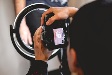 Young tattoo artist girl taking a photo of a new tattoo of yin yang with white ink in the hand of a guy in front of a led ring