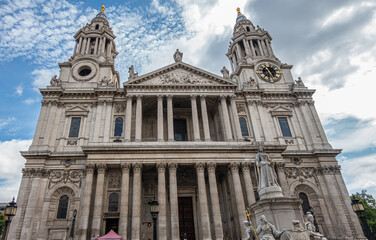 Fototapeta na wymiar London, England, UK - July 6, 2022: St. Paul's Cathedral. Gray stone front west facade with 2 towers, Corinthian columns on 2 levels, sculpted pediment and clock under blue cloudscape