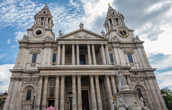London, England, UK - July 6, 2022: St. Paul's Cathedral. Gray stone front west facade with 2 towers, Corinthian columns on 2 levels, sculpted pediment and clock under blue cloudscape
