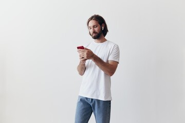 Man blogger holds a phone in his hands and communicates with people online in social networks with a smile and a white t-shirt on a white background