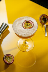Glass of Porn Star Martini cocktail with passionfruit on yellow table with dark background, raw...