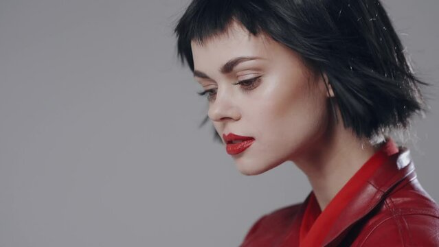 Beauty portrait of a fashion model with beautiful make-up with red lips and in a red cloak moves looking at the camera with her eyes.