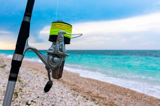 Fishing reel with green fishing line on the seashore. Sea fishing.