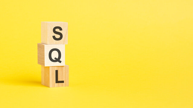 SQL - Structured Query Language - text on wooden block with yellow background.
