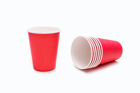 Red disposable cardboard cups on a white background in the center of the image. One disposable red cup and a set of clean and ready-to-use disposable cups lie on a white background