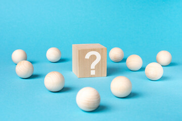 wooden cube with a question mark surrounded by wooden balls on a blue table background