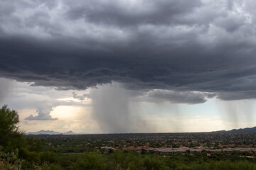 Naklejka na ściany i meble Monsoons in the Sonoran Desert with rain shafts or curtains coming down out of heavy dark gray clouds. Beautiful summer storm activity in the American Southwest. Pima County, Oro Valley, Arizona, USA.
