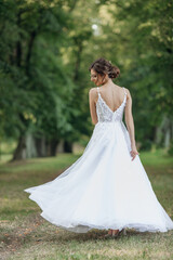 Rearview vertical portrait young pretty, shy, shiny bride with hair bun swirling around in white wedding dress in park