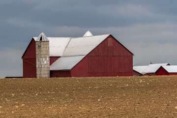 Red barn and silo on an Amish farm surrounded by a freshly planted field under a dark cloudy sky   Holmes County, Ohio © Seth