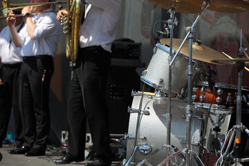 Fototapeta na wymiar A drum kit and a group of professional musicians in festive clothes playing brass musical instruments standing in a row on a stage outdoors on a summer day