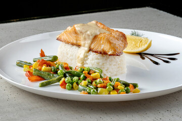 Bowl of rice with vegetables and salmon. Dish poured with sauce, macro photography.