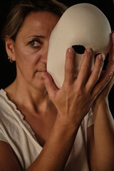 a young woman with a white theatrical mask in her hands
