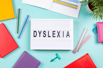 Dyslexia awareness, help children with reading, learning difficulties concept. Lightbox with DYSLEXIA word, colorful books and open book with reading highlight bookmark overlays strips. Top view