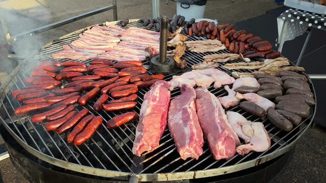 Fresh meat placed on giant circular grill ready to be cooked barbecue style. Slow motion video of a fairground food stand composed of chorizos, black pudding, ribs, chicken and sirloin steak