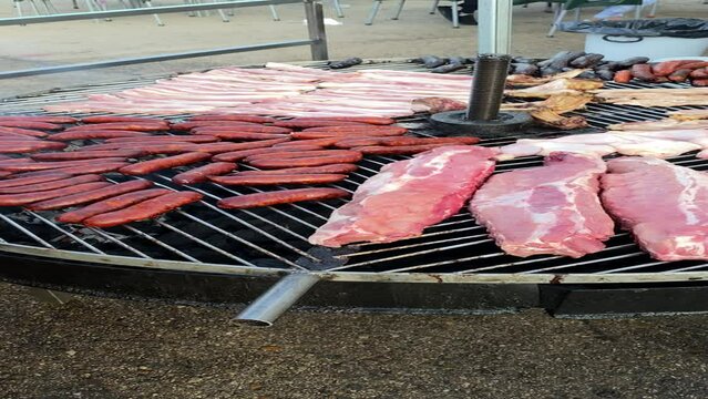 Fresh meat placed on giant circular grill ready to be cooked barbecue style. Slow motion vertical video of a fairground food stand composed of chorizos, black pudding, ribs, chicken and sirloin steak