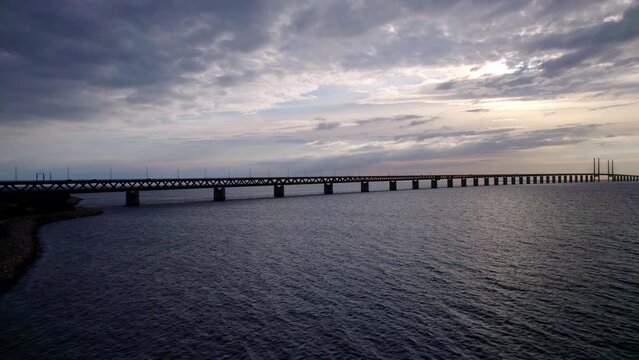 Golden hour view from low angle on the &Ouml;resund bridge near Malm&ouml; Sweden to Copenhagen Denmark. Slowly towards the sunset over waves on the &Ouml;resund strait, with a wind farm in the sea behind the bridge