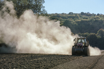 un tracteur qui laboure avec un muage de poussière