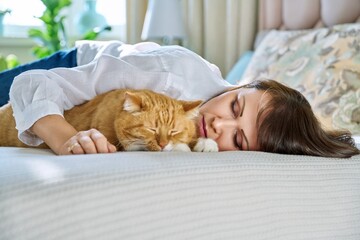 Middle aged woman sleeping with big ginger cat on bed