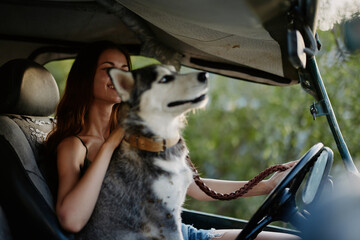 A woman rides in a car with her husky dog ​​and smiles while traveling by car to nature in the forest in summer. Lifestyle on the road by car with a dog