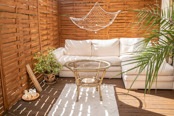 Real photo of relaxing boho zone in home. Wooden floor on terrace with comfy furniture and green...