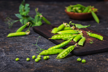 Green peas in pods on a stone surface, low key photography with selective focus