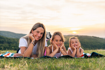 portrait of happy mother and daughters smiling and laughing lying on blanket in park, they posing for photo.