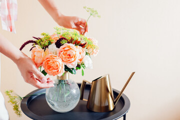 Close up of fresh english roses Lady of Shallott. Woman makes bouquet in vase of orange flowers on table at home. © maryviolet