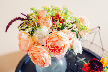 Fresh bouquet of roses zinnia amaranth flowers put in vase on table. Process of arranging with basket and pruner