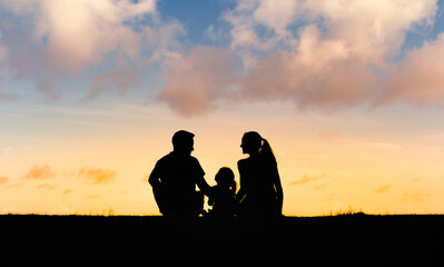 silhouette of a family parents and child sitting in nature watching the sunset