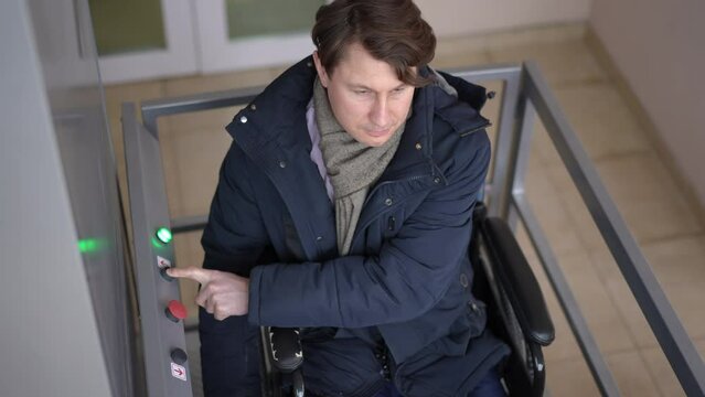 High angle view portrait of Caucasian man in wheelchair pressing button moving up on lift platform for people with disabilities. Confident ill guy using accessibility device indoors in building