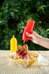 Agregando salsa al Pollo firto con tajadas servido en una canasta de plastico
