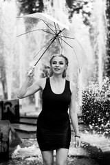 Happy woman having fun at the city fountain on a summer day with a transparent umbrella.
