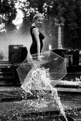 Obraz premium Happy woman having fun at the city fountain on a summer day with a transparent umbrella.