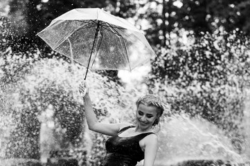 Happy woman having fun at the city fountain on a summer day with a transparent umbrella.