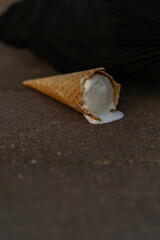 Ice cream in a waffle cone melts on the pavement.