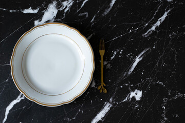 Empty plate with golden fork on a dark granite background with copy space. Top table view. Biblical fasting, Atonement Day, weight-loss, diet restrictions concept.