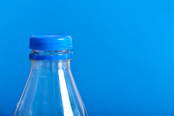 Top of an empty plastic transparent disposable bottle with blue cap and blue background. Concepts: sustainability, recycling, pollution, zero waste campaigns.