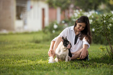 Portrait of young woman petting and hugging her dog (french bulldog) in the park