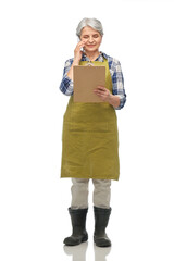 gardening, farming and old people concept - portrait of smiling senior woman in green garden apron and rubber boots with clipboard calling on smartphone over white background