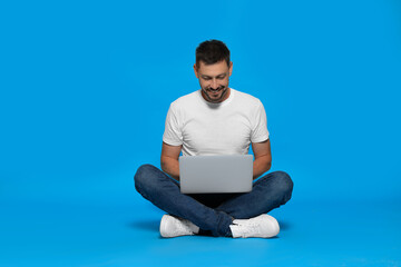 Happy man sitting with laptop on light blue background