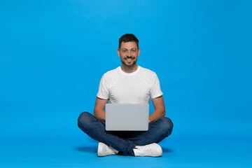 Happy man sitting with laptop on light blue background