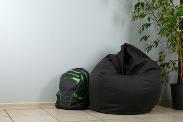 Black bean bag chair, houseplant and backpack near light grey wall in room. Space for text