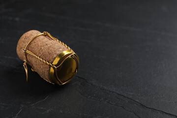 Cork of sparkling wine and muselet cap on black table. Space for text